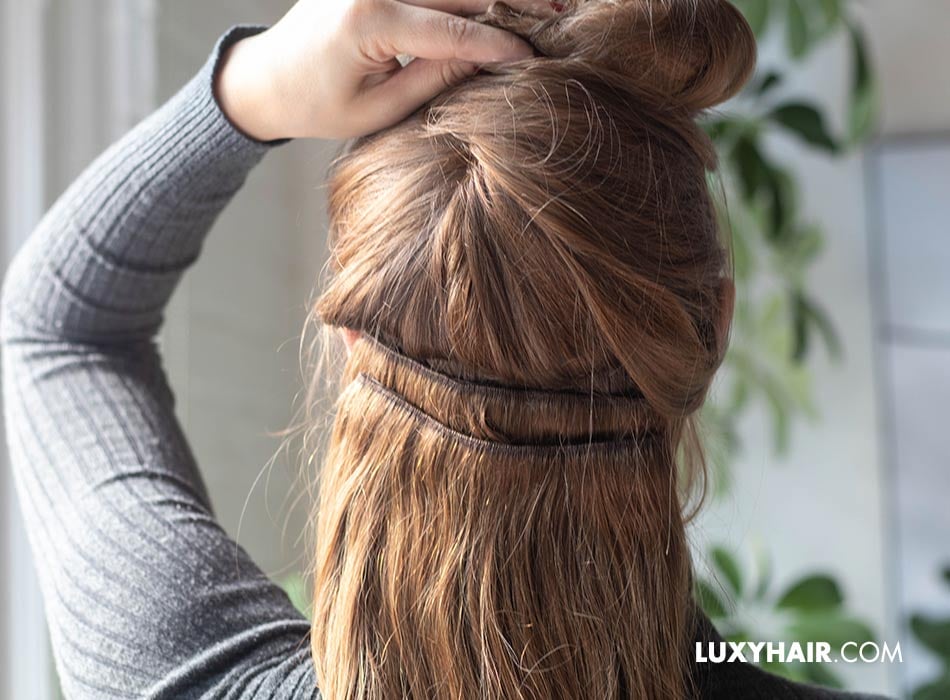 A woman with hair extensions putting her hair up to show the weft hair extensions.