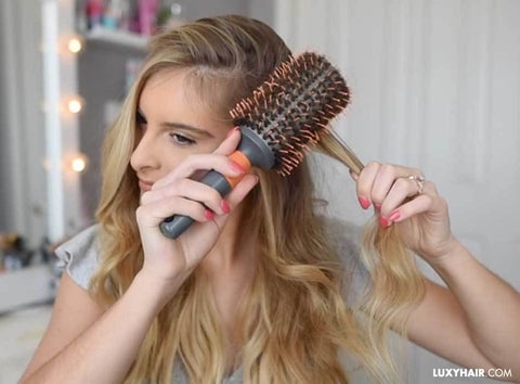 A woman is brushing her hair extensions with a brush.