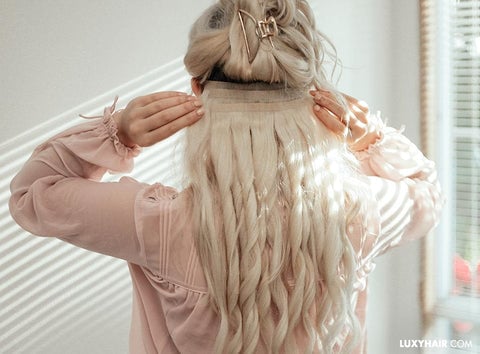 Woman installing blonde hair extensions in front of a sunlit window