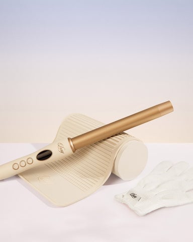 A gold hair curling wand and a heating pad protector with gloves placed side by side on a surface.