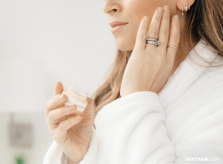 A woman holding a cream and applying it on her face.