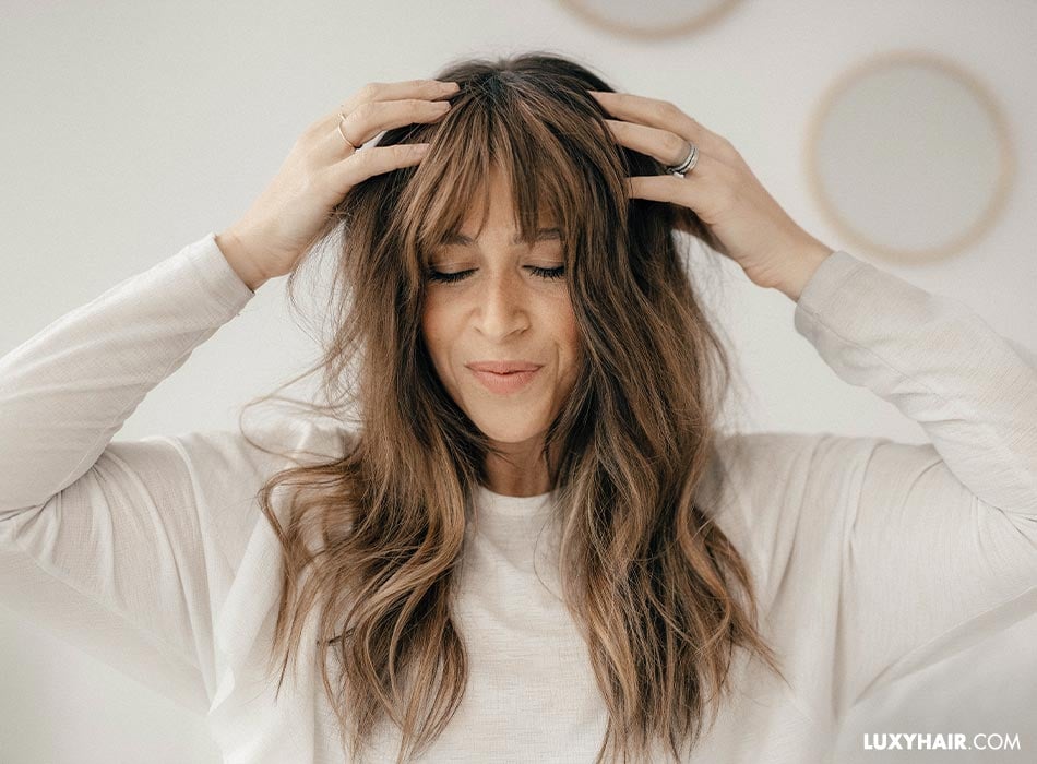 A woman with long brown wavy hair extension using her hands to tease the hair.