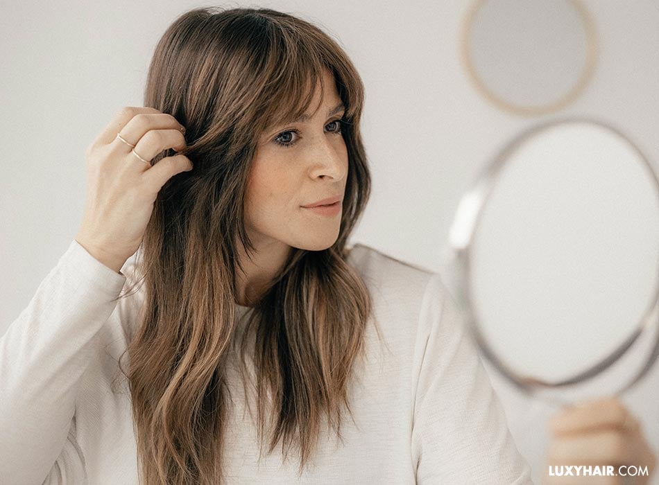A woman with her hand on her hair and looking at herself in front of the mirror.