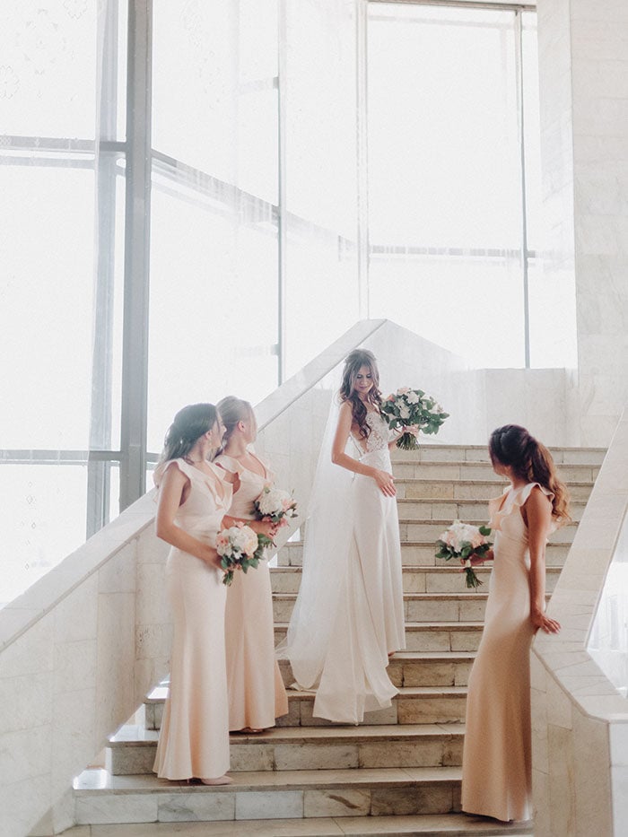 Bridesmaids in blush dresses standing on stairs. Good Wedding hair tips for brides.