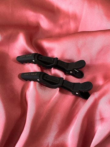 Two black hair clips on a pink satin cloth.